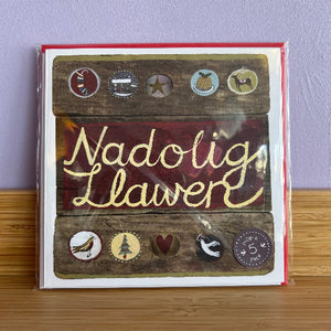 Card with 'Nadolig Llawer' text and decorative elements on a wooden surface.