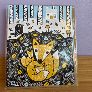 Packaged illustration of a fox family with a bird and trees on a card.